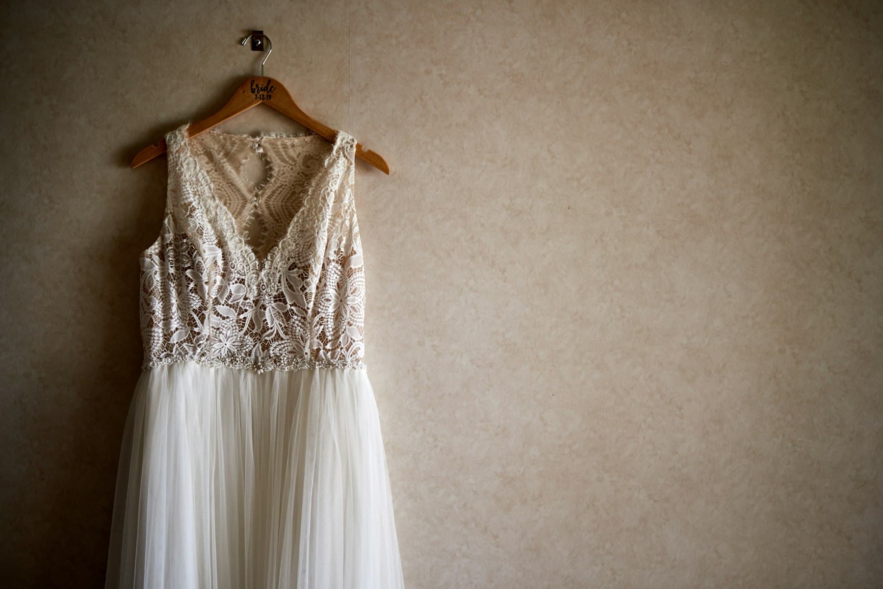 Vestido de renda floral com decote em V e saia de tule, pendurado num cabide de madeira
